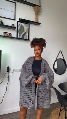 a woman standing in front of a white wall wearing a gray crochet cardigan