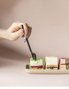 a person is holding a fork and cutting into small desserts on a plate with three different types of cakes