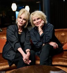 two women sitting next to each other on top of a brown couch in a living room