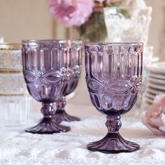 three glass goblets sitting on a table with pink flowers in the back ground