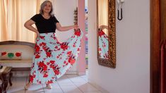 a woman in a black shirt is holding a red and white flowered skirt while standing next to a mirror