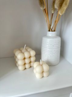 two white vases with dried flowers in them on a shelf next to some candles