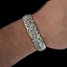 a man's arm wearing a silver bracelet with intricate designs on the clasps