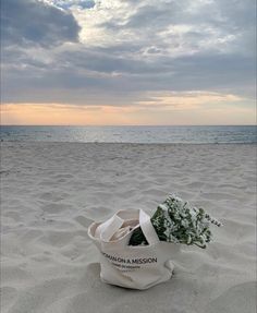 a white bag with flowers sitting on top of it in the sand at the beach