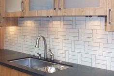 a kitchen with black counter tops and white tile backsplash, stainless steel faucet