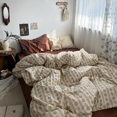 an unmade bed sitting next to a window covered in blankets and pillowcases