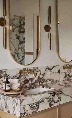 a bathroom with marble counter tops and gold fixtures on the wall, along with two round mirrors