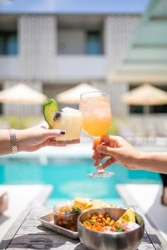 two people are toasting with drinks by the pool