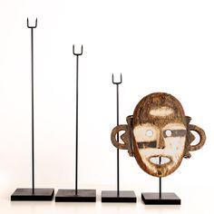 three metal sculptures with faces on them and one is wearing a face mask, the other has two poles