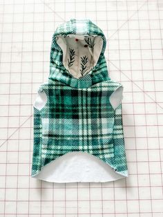 a green and white plaid dog hoodie on top of a piece of paper next to a ruler