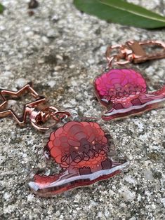 two pieces of glass with pink and red designs on them sitting on a rock next to leaves