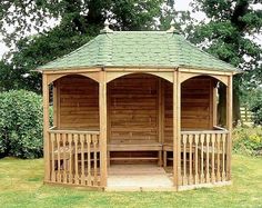 a wooden gazebo sitting on top of a lush green grass covered park bench next to a tree