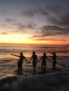 four people holding hands while standing in the water at sunset or dawn on an ocean beach