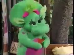 a green stuffed animal sitting on top of a pink vase next to a tree and fence