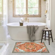 a white bath tub sitting under a window next to a rug on the bathroom floor