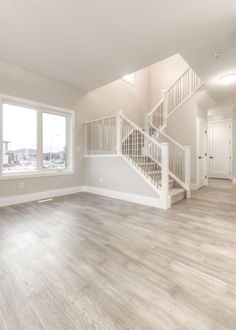 an empty living room with wood floors and white stairs in the center, leading to a second story window