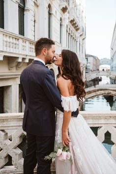 a bride and groom kissing in front of a bridge with flowers on it's side