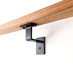 a close up of a wooden shelf with a metal hook attached to it and a white wall in the background