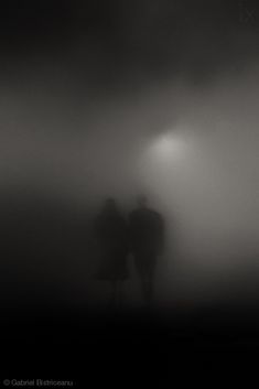 two people standing in the fog under a street light