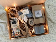 an open box with some items in it on a white blanket next to candles and lights