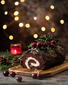 a chocolate roll decorated with cherries on a cutting board next to some christmas decorations