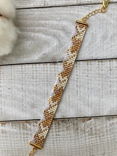 a gold and white beaded bracelet sitting on top of a wooden table next to a cotton