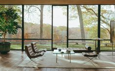 an open living room with large windows and furniture in front of the glass wall that overlooks trees