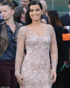 a woman in a dress is standing on the red carpet with other people behind her