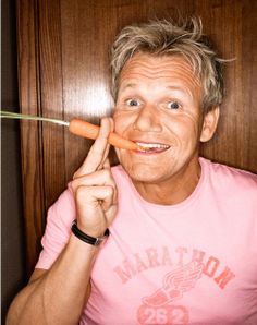 a man holding a carrot in front of his face and pointing to it with one hand