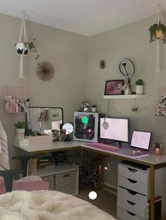 a desk with two computer monitors on top of it next to a bed in a room