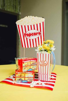 popcorn buckets with flowers in them sitting on a yellow table cloth next to boxes of popcorn