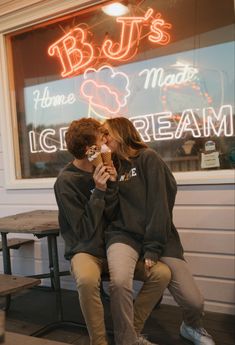 two people sitting in front of a store window eating ice cream and kissing each other