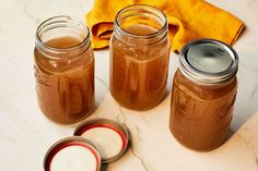 three jars filled with brown liquid sitting on top of a white marble counter next to a yellow towel