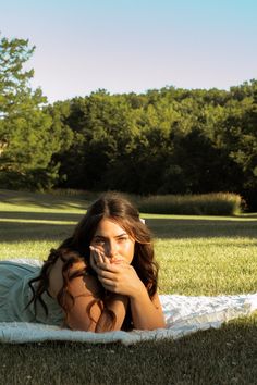 a beautiful young woman laying on top of a white blanket in the middle of a field