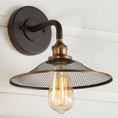 an old fashioned light fixture on the side of a white painted wall with a wire mesh shade