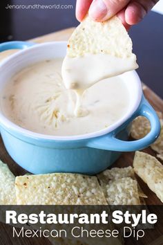 a hand dipping a tortilla chip into a blue bowl filled with mexican cheese dip