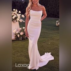 a woman in a white dress posing for a photo on the grass with flowers behind her