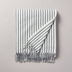 a white and black striped towel with tassels on the bottom, laying on a gray surface