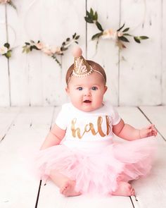 a baby girl wearing a pink tutu and a gold crown sits on the floor