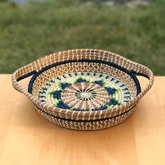 two woven baskets sitting on top of a wooden table next to grass and water in the background