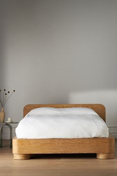 a bed sitting on top of a hard wood floor next to a white pillow and vase