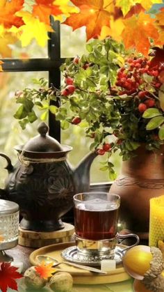 a table topped with cups and saucers covered in autumn leaves next to a vase filled with flowers