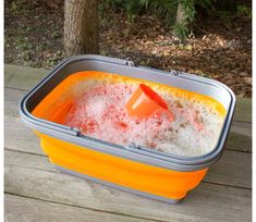 an orange and gray container filled with foam on top of a wooden table next to a tree