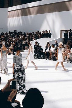 several models walk down the catwalk in front of a large crowd at a fashion show