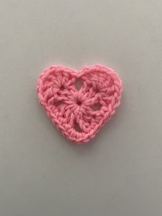 a pink crocheted heart on a white surface with the center in the shape of a flower