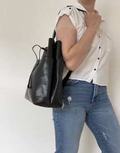 Thick glossy black leather bag with a sling style shoulder strap.  The strap is adjustable from 58-94 cm. Has two equally sized slim pockets on the front and back of the bag.  The main compartment at the top is open but has a drawstring fastening to secure somewhat the contents inside.  Theres one compartment inside with a small zipped pocket compartment.  The lining is a polyester manmade feel fabric in brown that has the bag makers name 'Elmani' woven into the fabric. Theres a fabric bade insi Modern Hobo Bag With Long Strap For Daily Use, Modern Hobo Bag With Long Strap For Travel, Leather Tote Shoulder Bag With Adjustable Straps, Leather Shoulder Bag Tote With Adjustable Straps, Leather Shoulder Bag With Adjustable Straps For On-the-go, Everyday Leather Bag With Long Strap, Modern Leather Shoulder Bag With Long Strap, Leather Shoulder Bag With Adjustable Straps For Everyday, Everyday Leather Shoulder Bag With Adjustable Straps