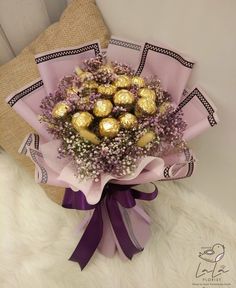 a bouquet of flowers with chocolates wrapped in purple ribbon on a white furnishing