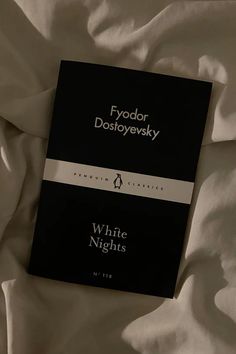 a black book laying on top of a white sheet covered bed next to a pillow