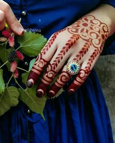 a woman's hands with henna and ring on her fingers, holding flowers