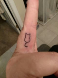 a person's hand with a small tattoo on the middle finger that has a cat head